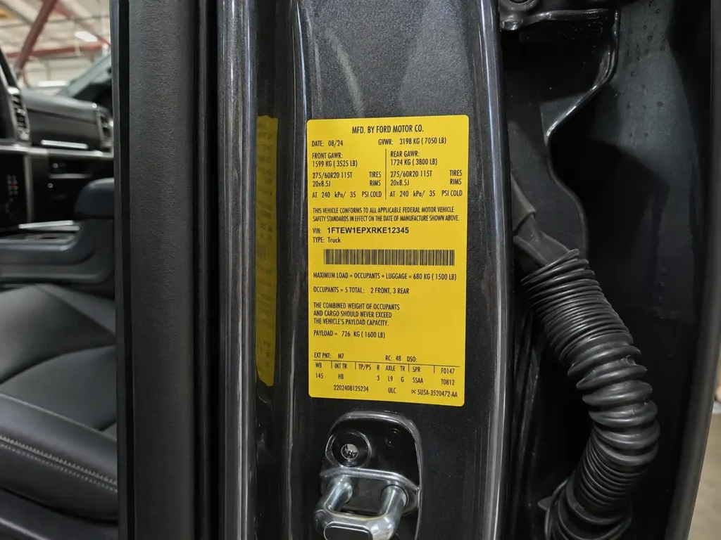 Close-up of a Ford F-150 driver-side door jamb showing the yellow payload and certification label sticker