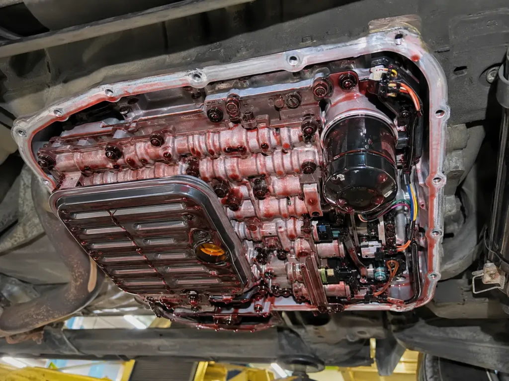 Exposed Ram 1500 RFE transmission valve body with sump filter and spin-on cooler return filter coated in red fluid