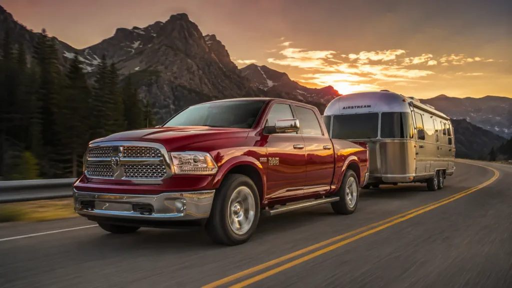 2013 Ram 1500 Laramie Crew Cab in deep cherry red towing a silver Airstream travel trailer through a winding mountain road at sunset.