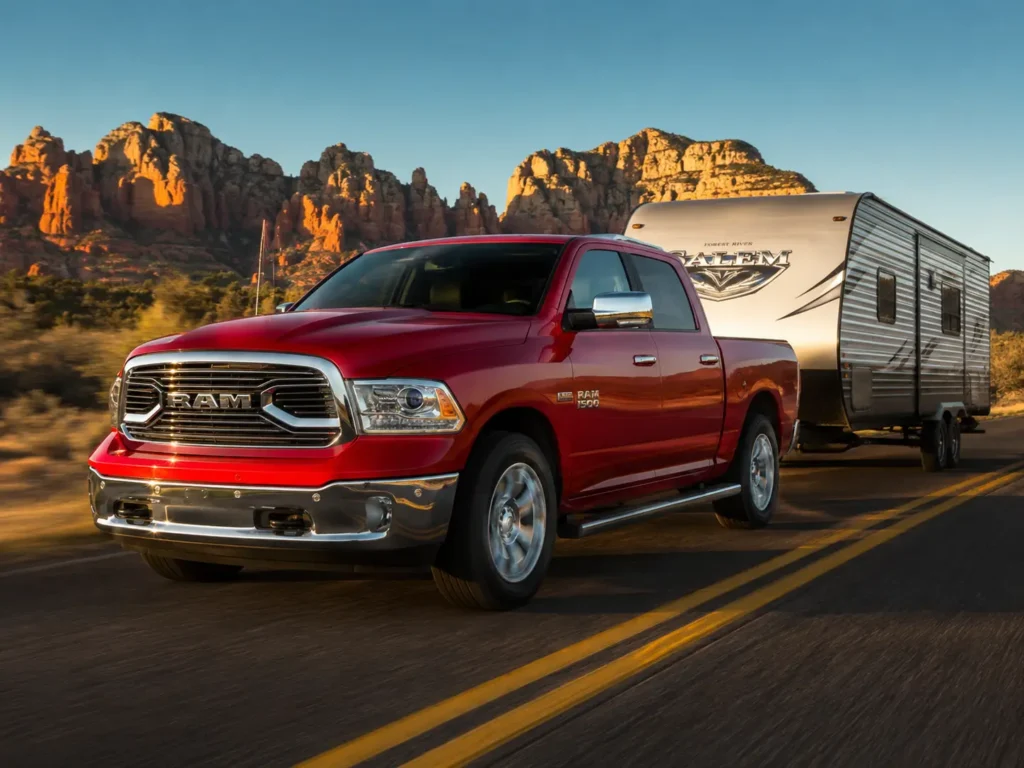 Flame Red 2018 Ram 1500 Crew Cab towing a large silver travel trailer on a desert highway, with red rock formations and golden-hour light in the background.